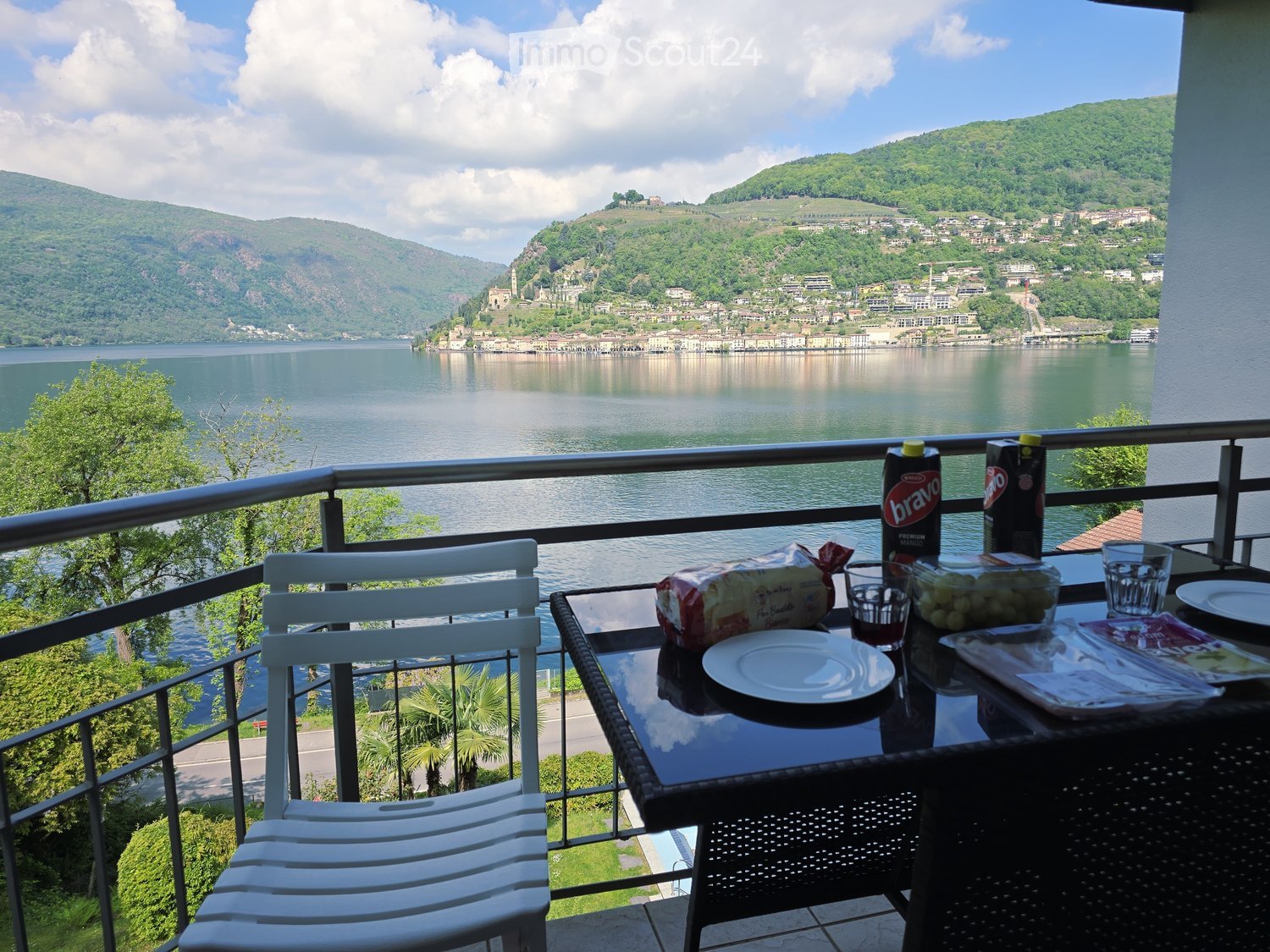 Balcony / Terrace. Balcony with a scenic lake view, featuring a table with chairs, a bottle, bread, and a cup.