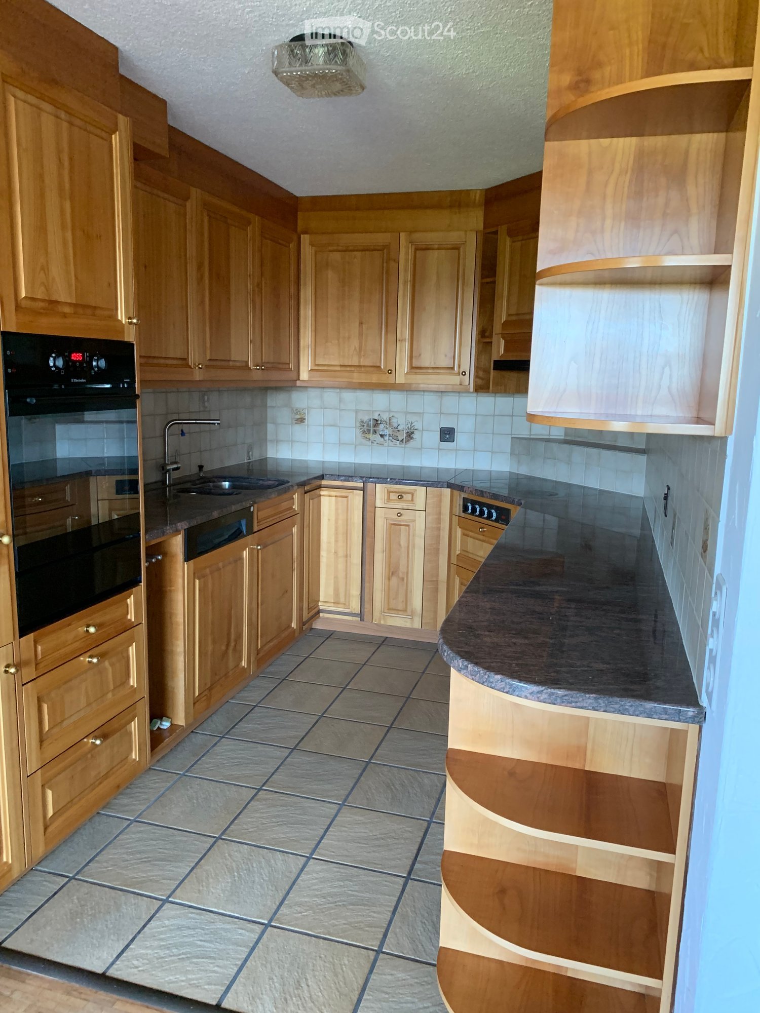 Kitchen. A well-lit kitchen with wooden cabinets, granite countertops, and tiled flooring. Features include an oven, sink, and faucet.