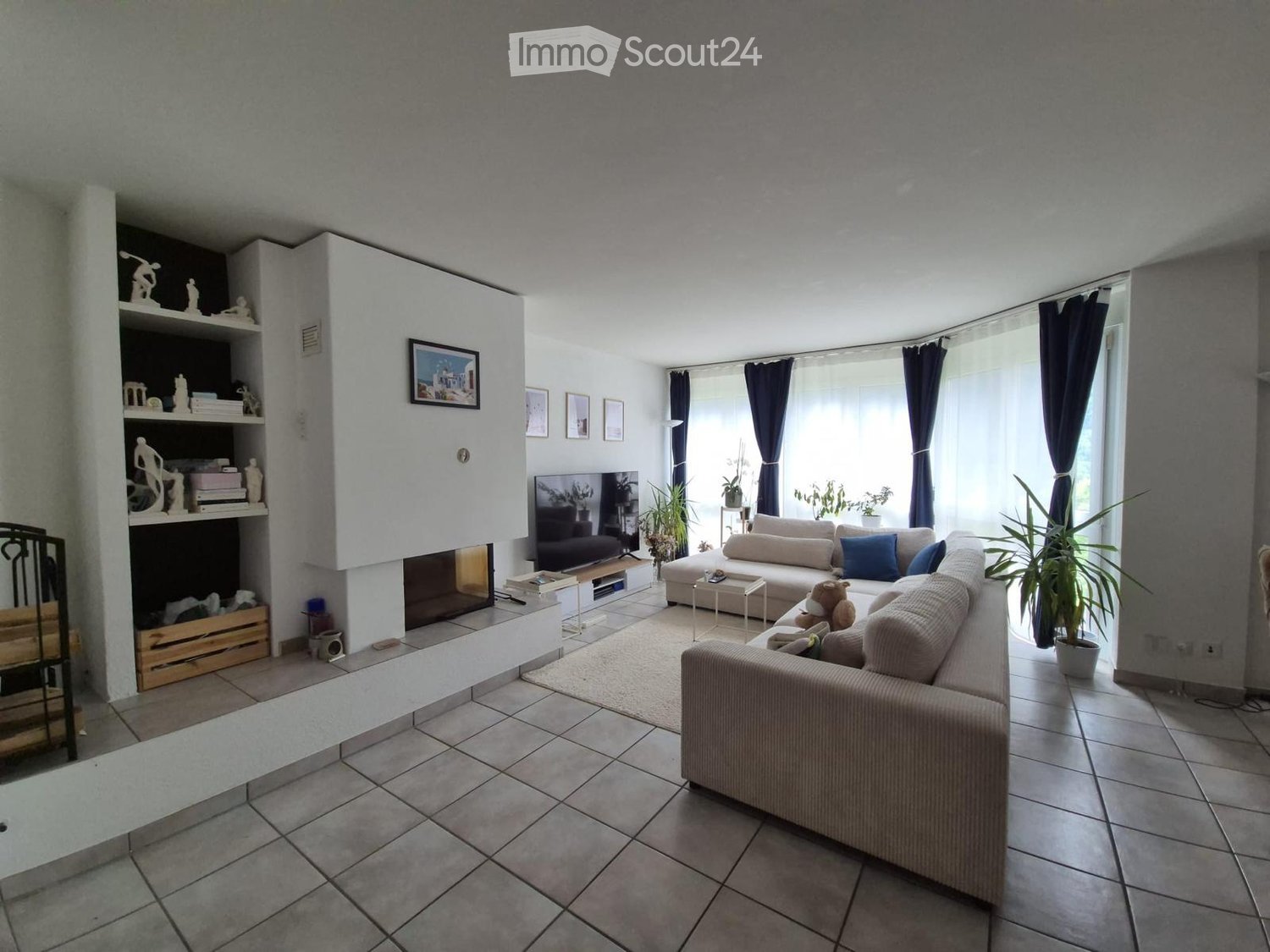 Living Room. Modern living room with tiled flooring, large windows, fireplace, sofa, coffee table, shelves, and decorative items.
