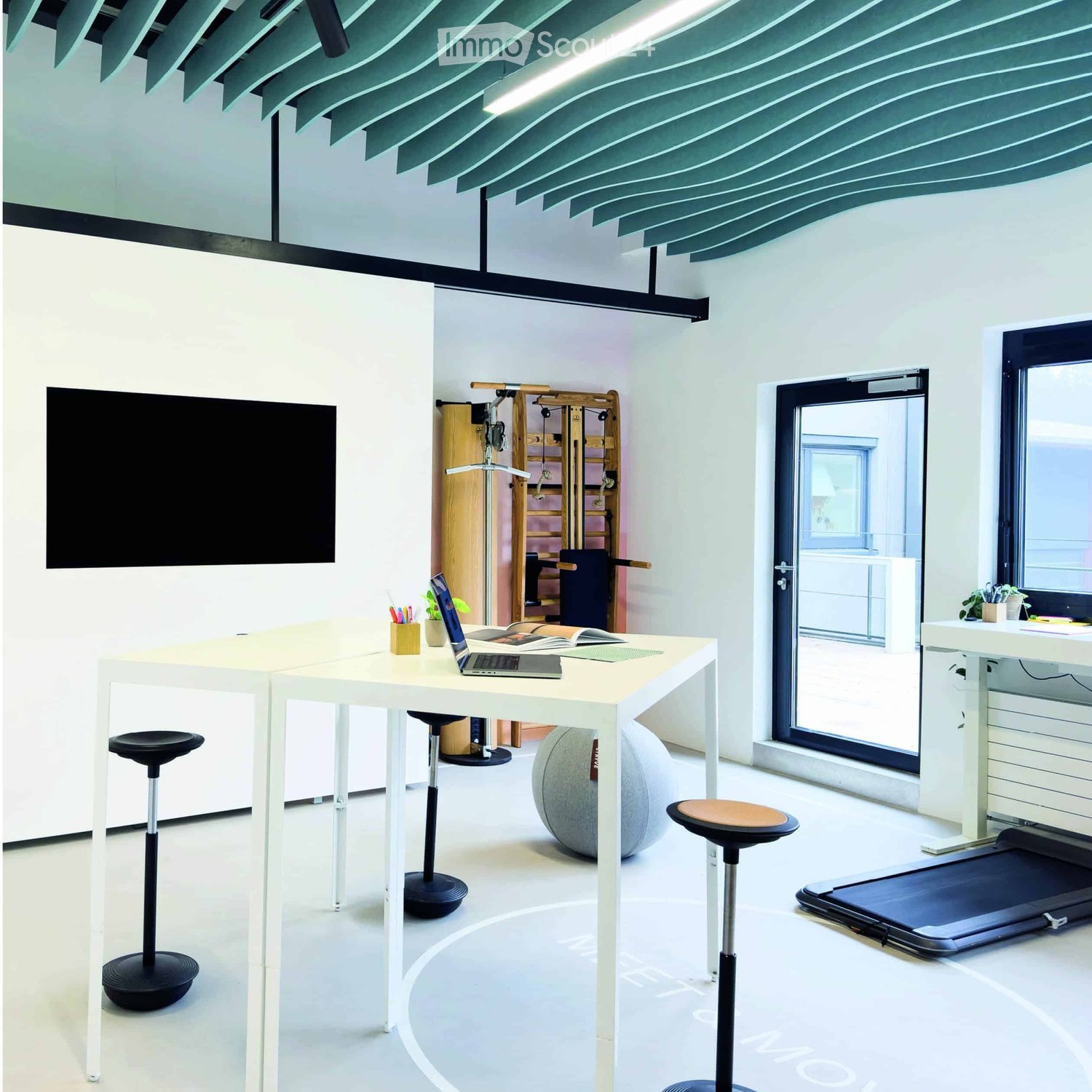 Furnished Room. Modern office space with white tables, laptop, stools, a large screen, a ball chair, and a treadmill.