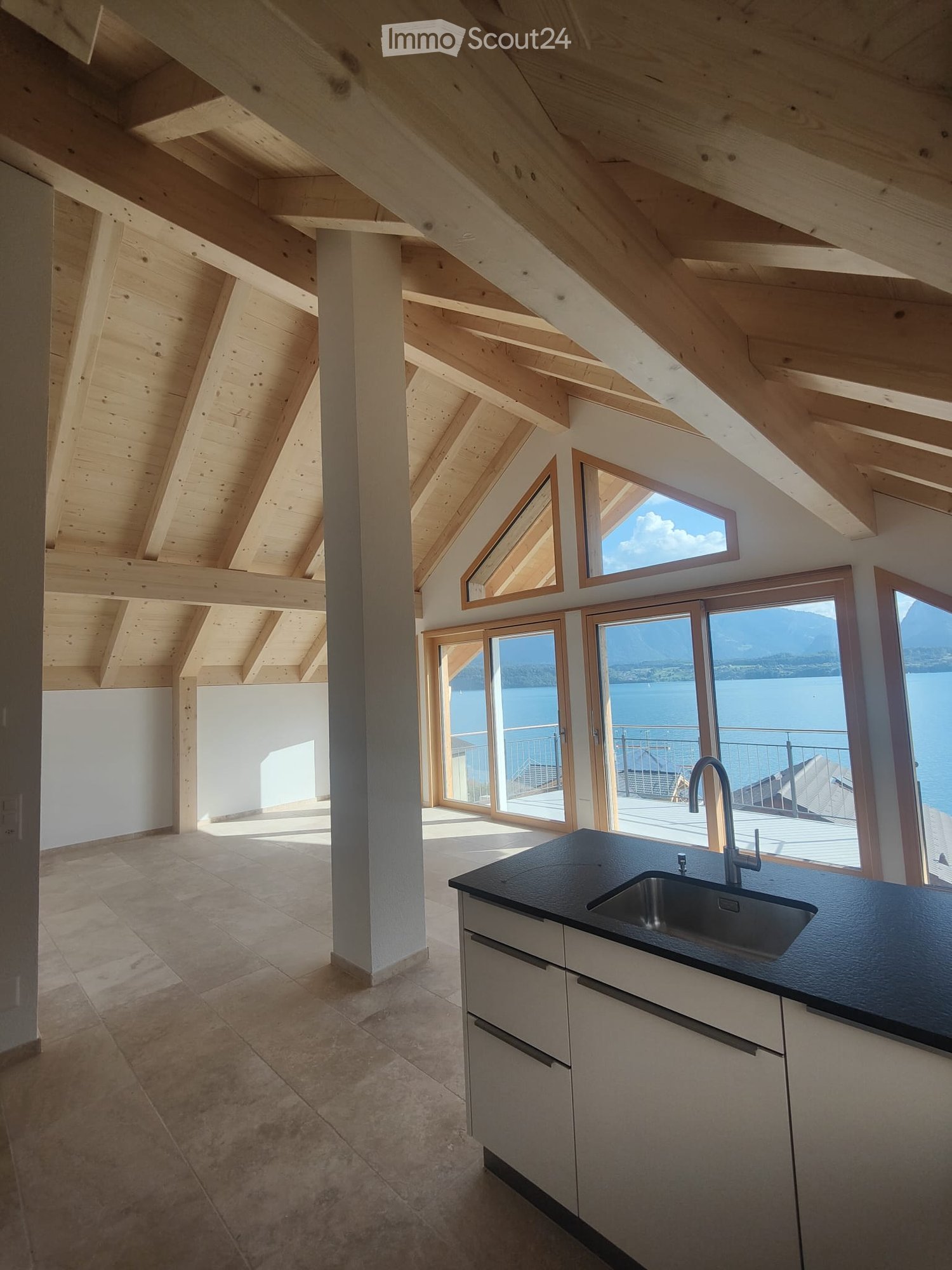 Kitchen. Modern kitchen with exposed wooden beams, large windows offering a scenic view, and a sleek black countertop with a stainless steel sink.