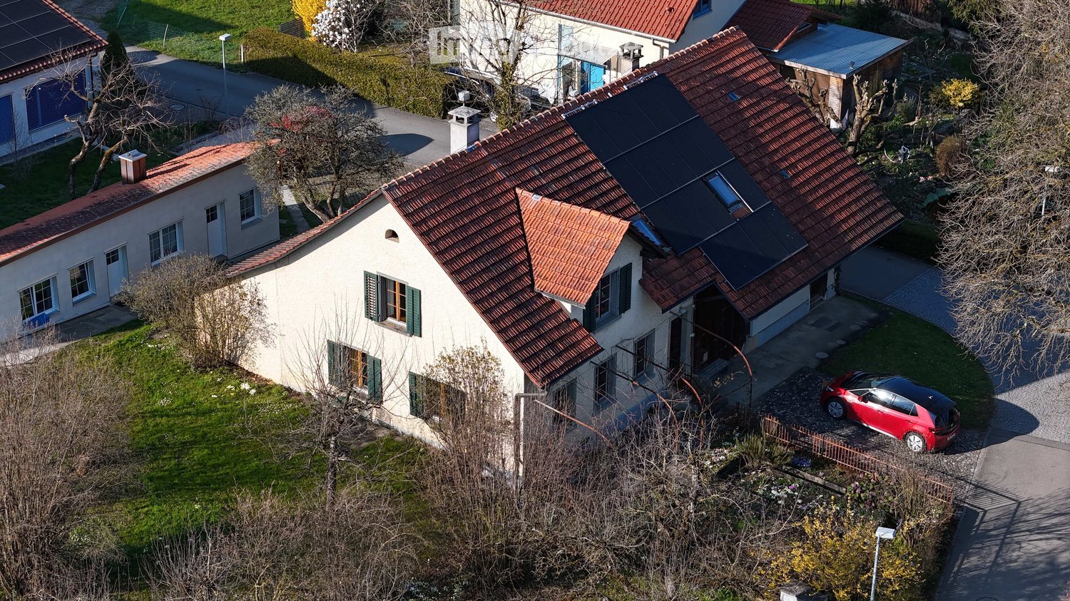 House. Aerial view of a two-story house with red-tiled roof, solar panels, and a red car parked in the driveway.