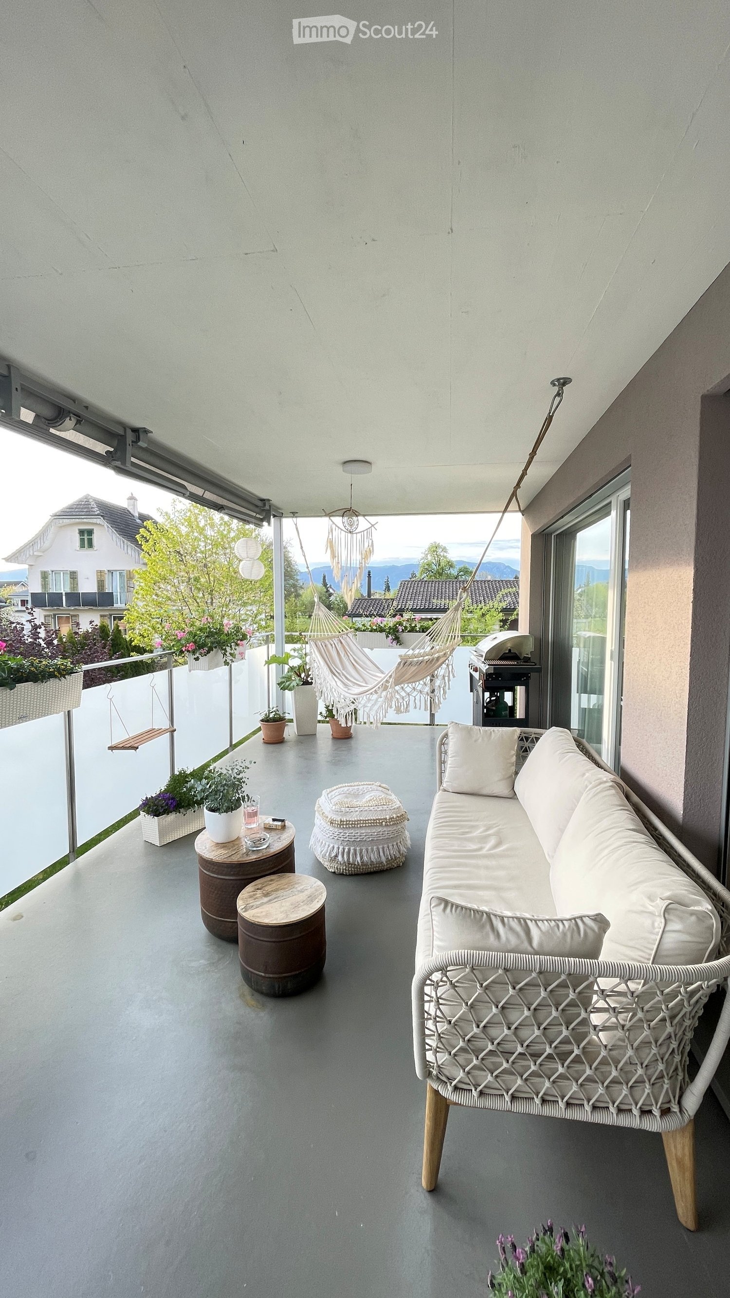Balcony with white couch, hammock, wooden tables, potted plants, and a swing