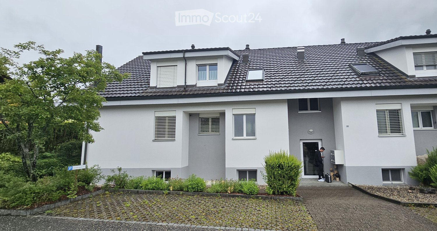 House. Two-story house with white exterior, grey roof, multiple windows with shutters, small garden, and a driveway.