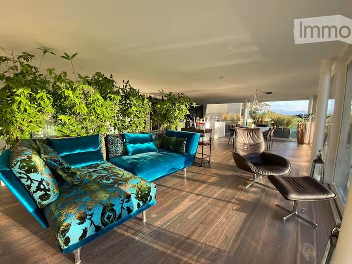 Furnished Room. Bright, modern living space with large windows offering a scenic view, featuring a blue sofa, matching cushions, a sleek chair, a small table, and a chandelier.
