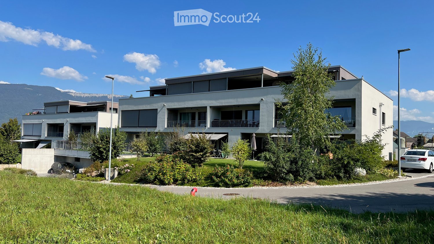 Building. Modern two-story building with large windows, balconies, and a landscaped garden area with trees and shrubs.