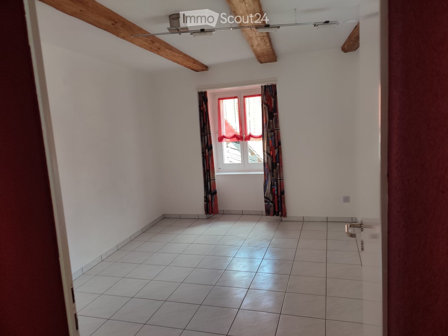 Unfurnished Room. Empty room with tiled floor, white walls, exposed wooden beams, and a window with red curtains.