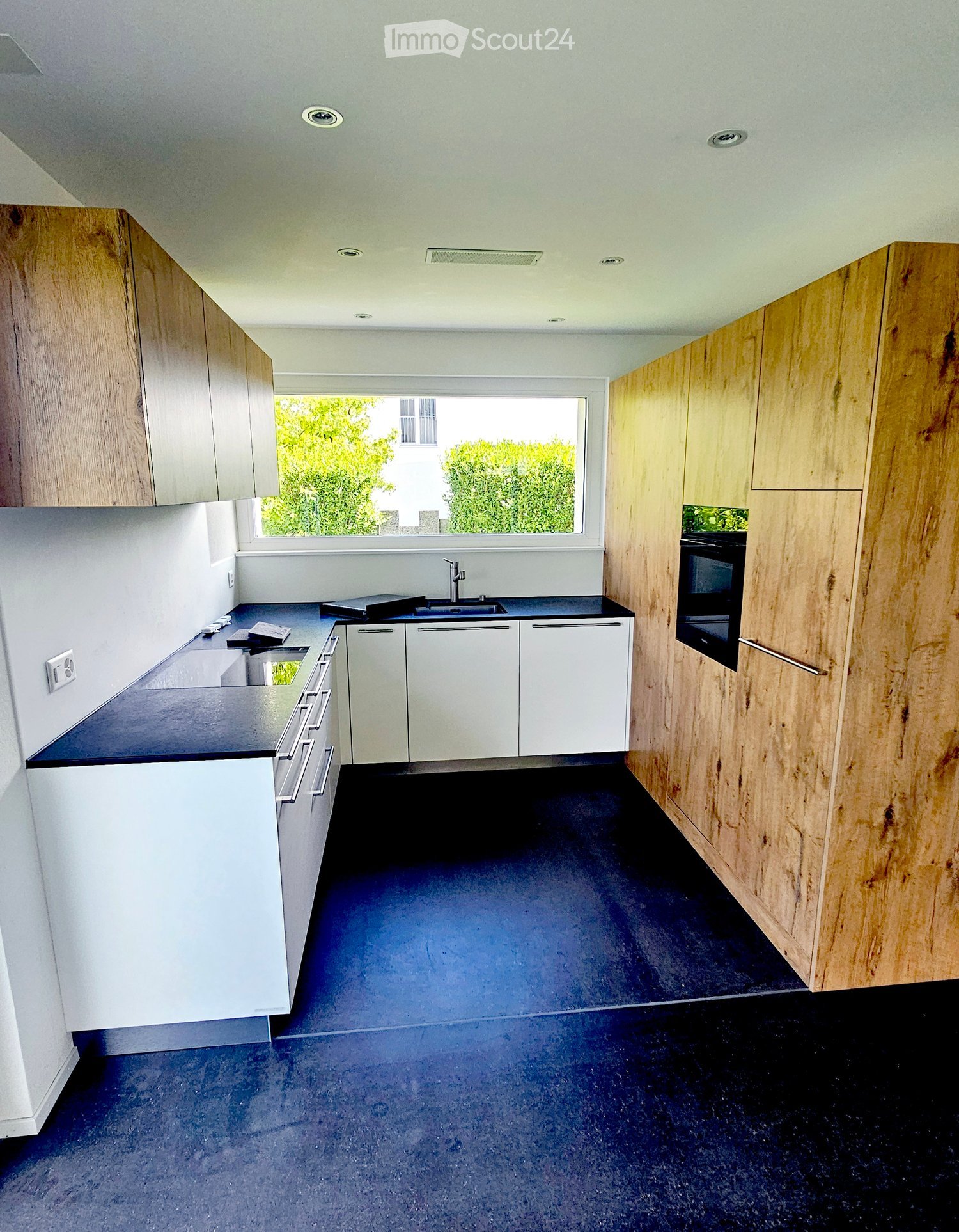 Kitchen. Modern kitchen with white and light wood cabinets, dark countertops, and a dark blue floor. Features a sink, oven, and ample storage space.
