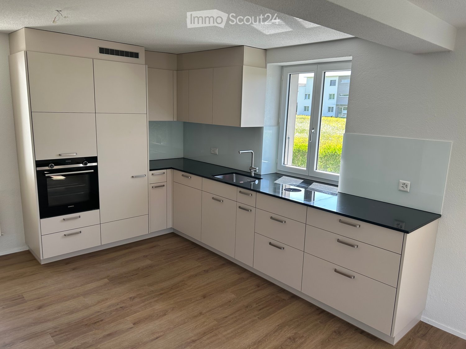 Kitchen. Modern kitchen with light-colored cabinets, black countertop, stainless steel sink, and built-in oven. Features wooden flooring and large windows.