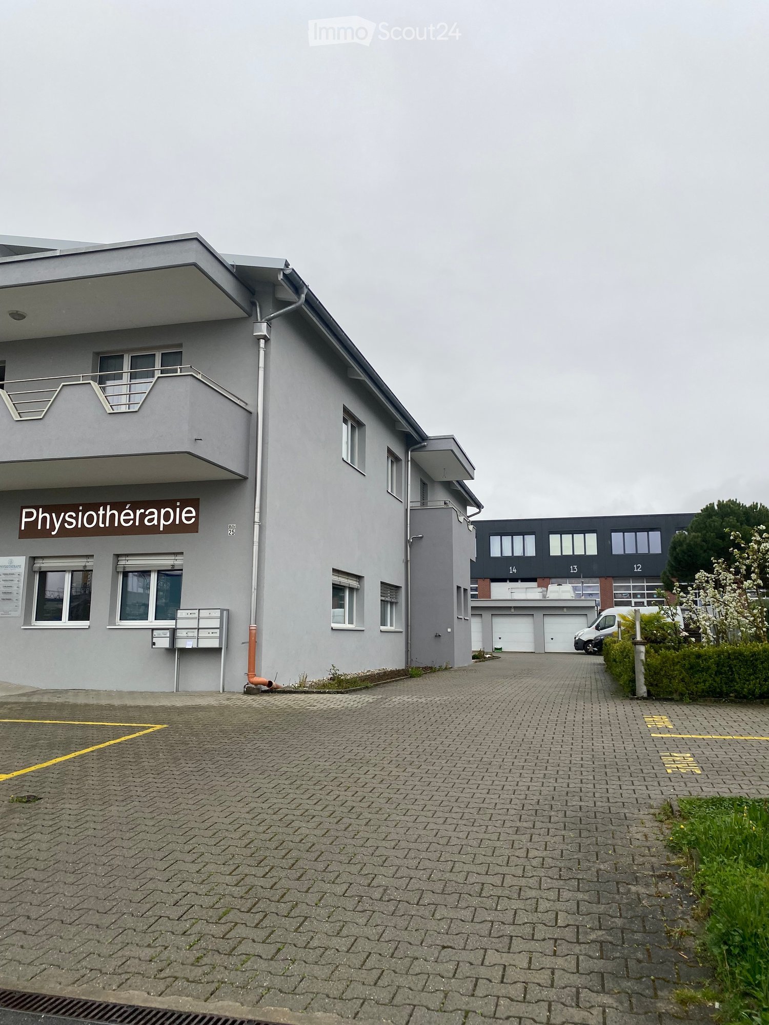 Building. Two-story building with grey exterior, balcony, and sign reading "Physiothérapie".