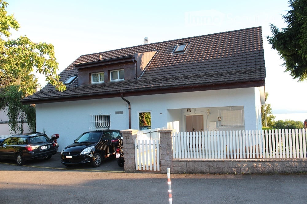 House. Two-story house with a tiled roof, white exterior, and a small garage. There are two parked cars and a scooter in front of the house.