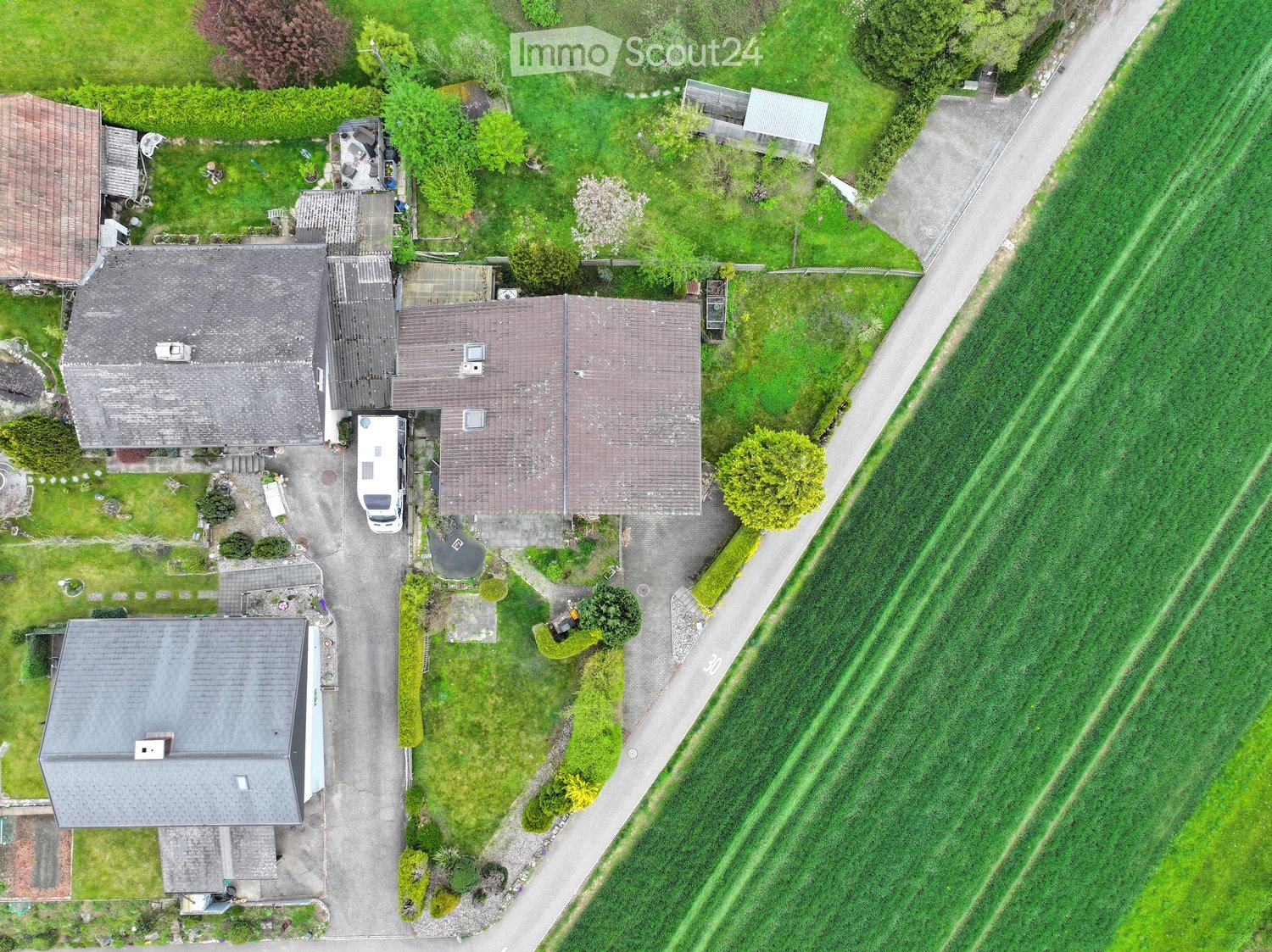 House. Aerial view of a residential property with multiple houses, driveway, and surrounding greenery.