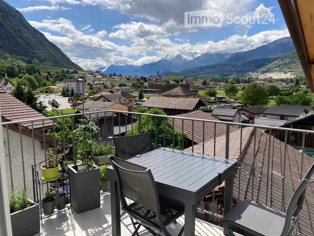 Balcony / Terrace. Balcony with a table, chairs, and potted plants, overlooking a scenic mountain town.