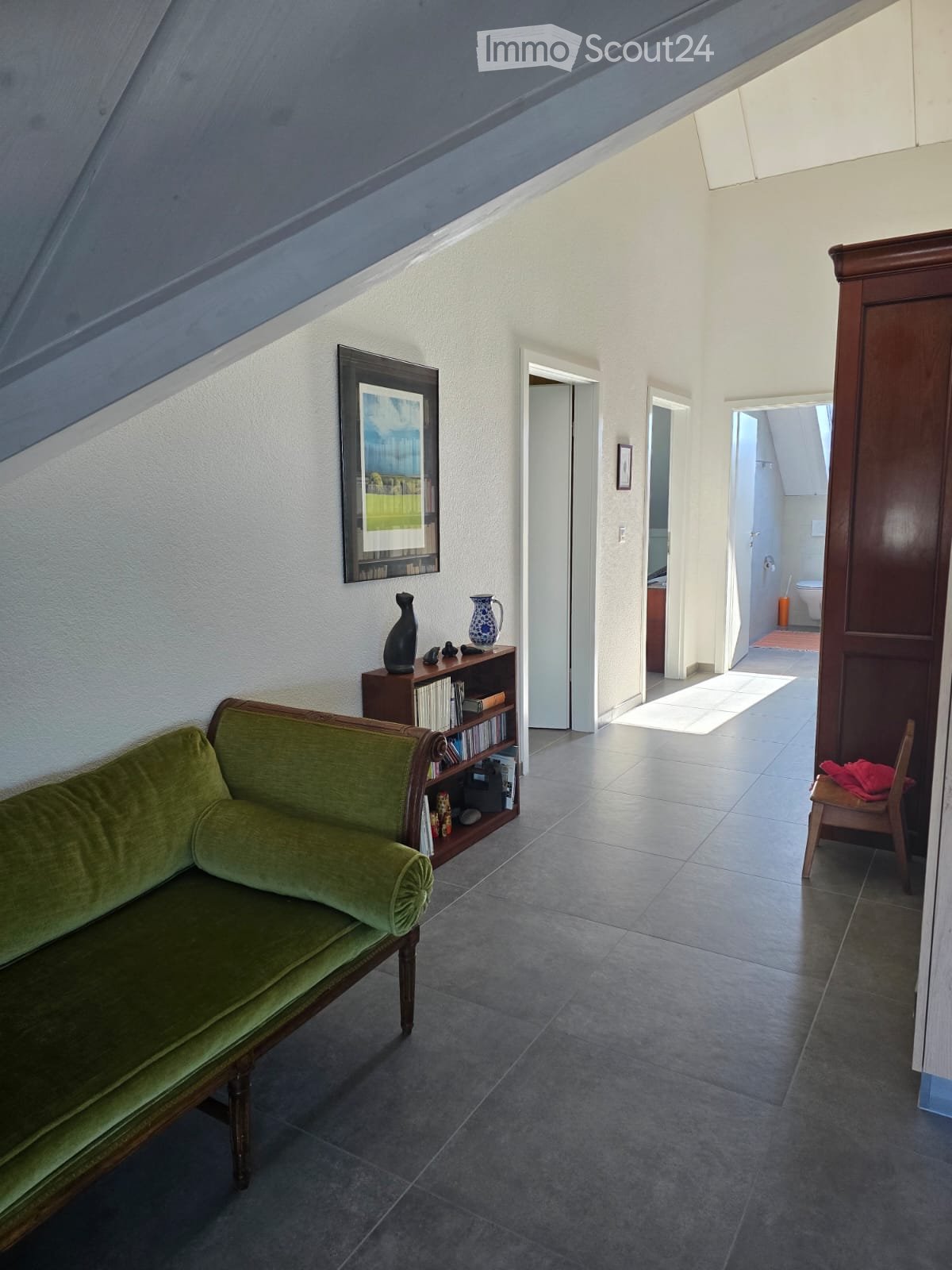 Furnished Room. Green sofa, wooden bookshelf with books and decorative items, small wooden chair, and a framed picture on the wall.