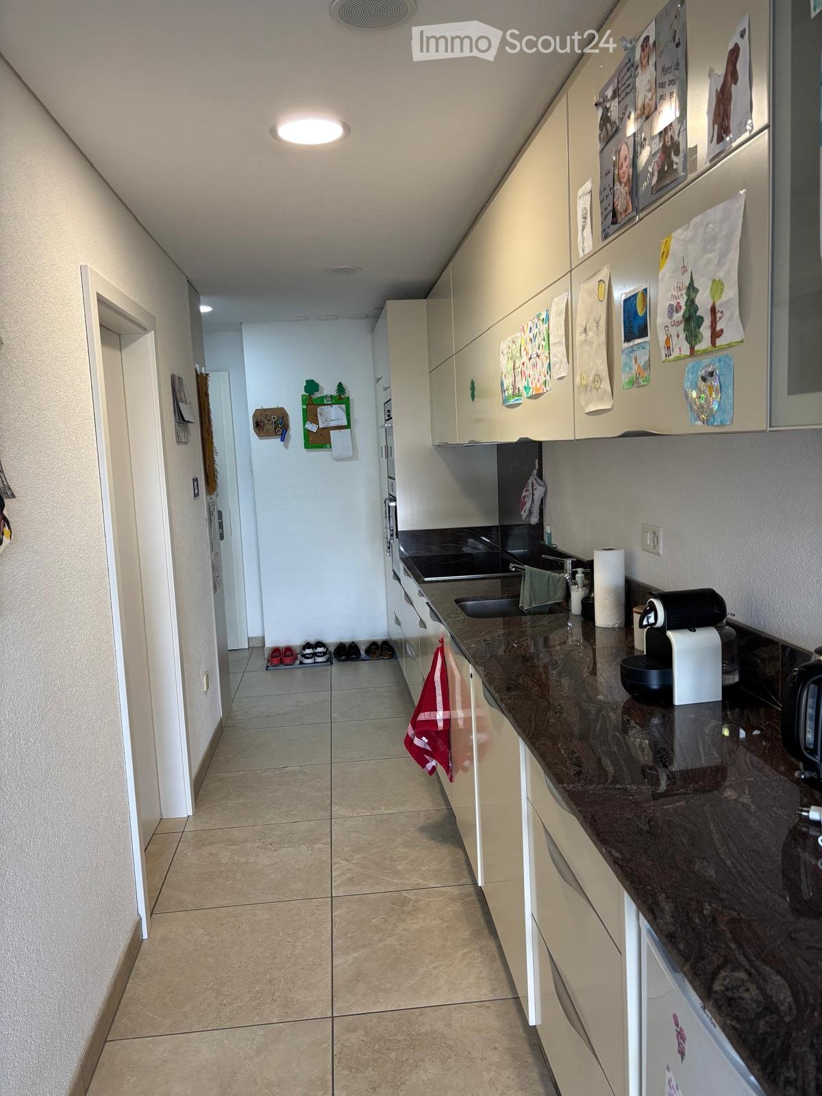 Kitchen. Modern kitchen with light-colored cabinets, granite countertop, sink, coffee maker, and various small appliances. The space is clean and organized with a hallway leading to another room.