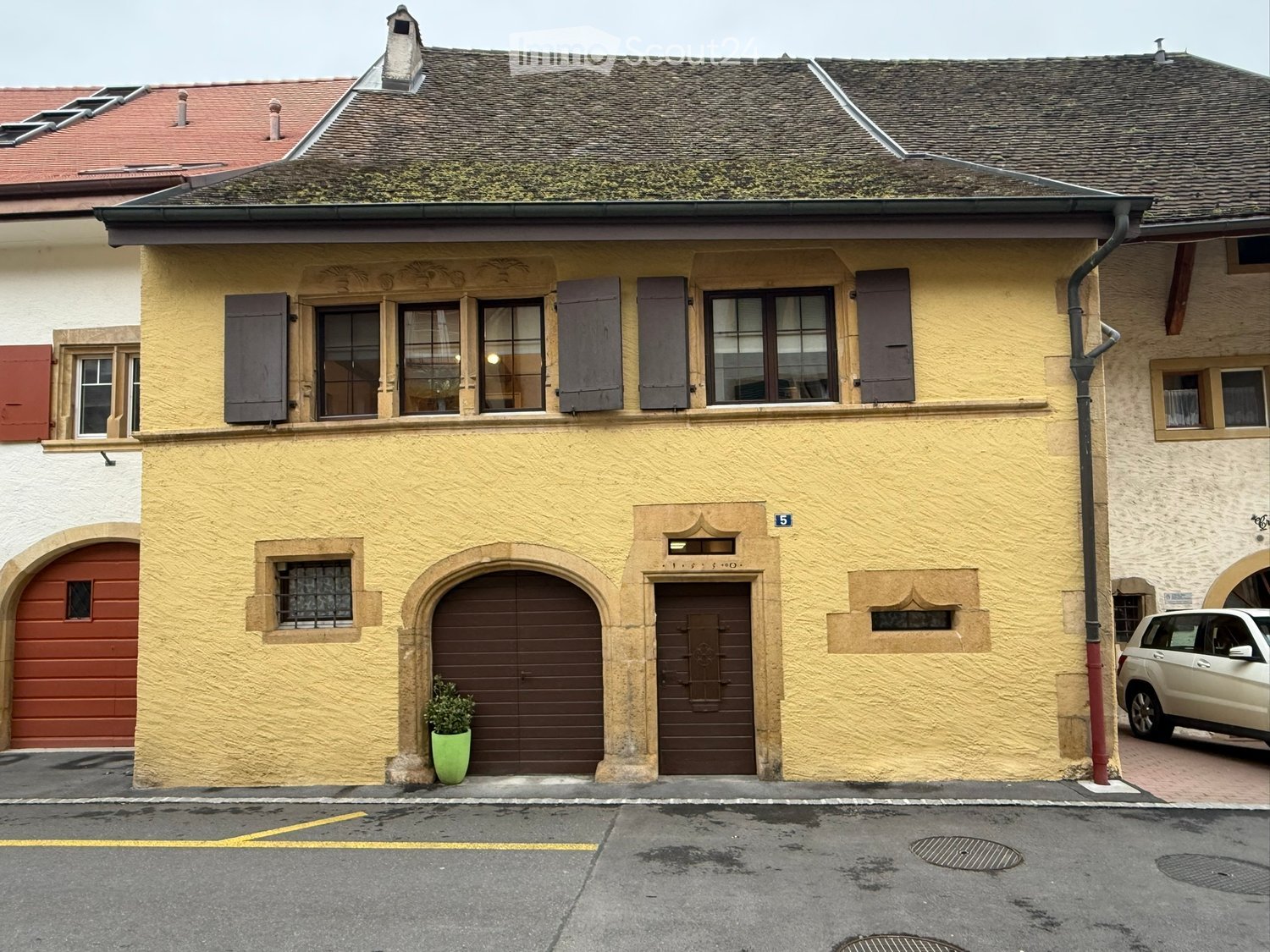 Building. Two-story building with yellow facade, multiple windows with shutters, garage, and entrance door.