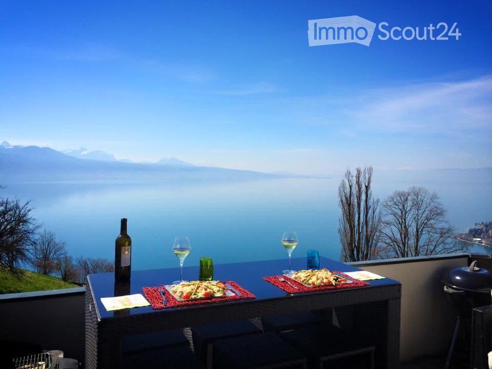 Balcony / Terrace. Balcony with a scenic lake and mountain view, featuring a table set for two with wine, plates of food, and cutlery.