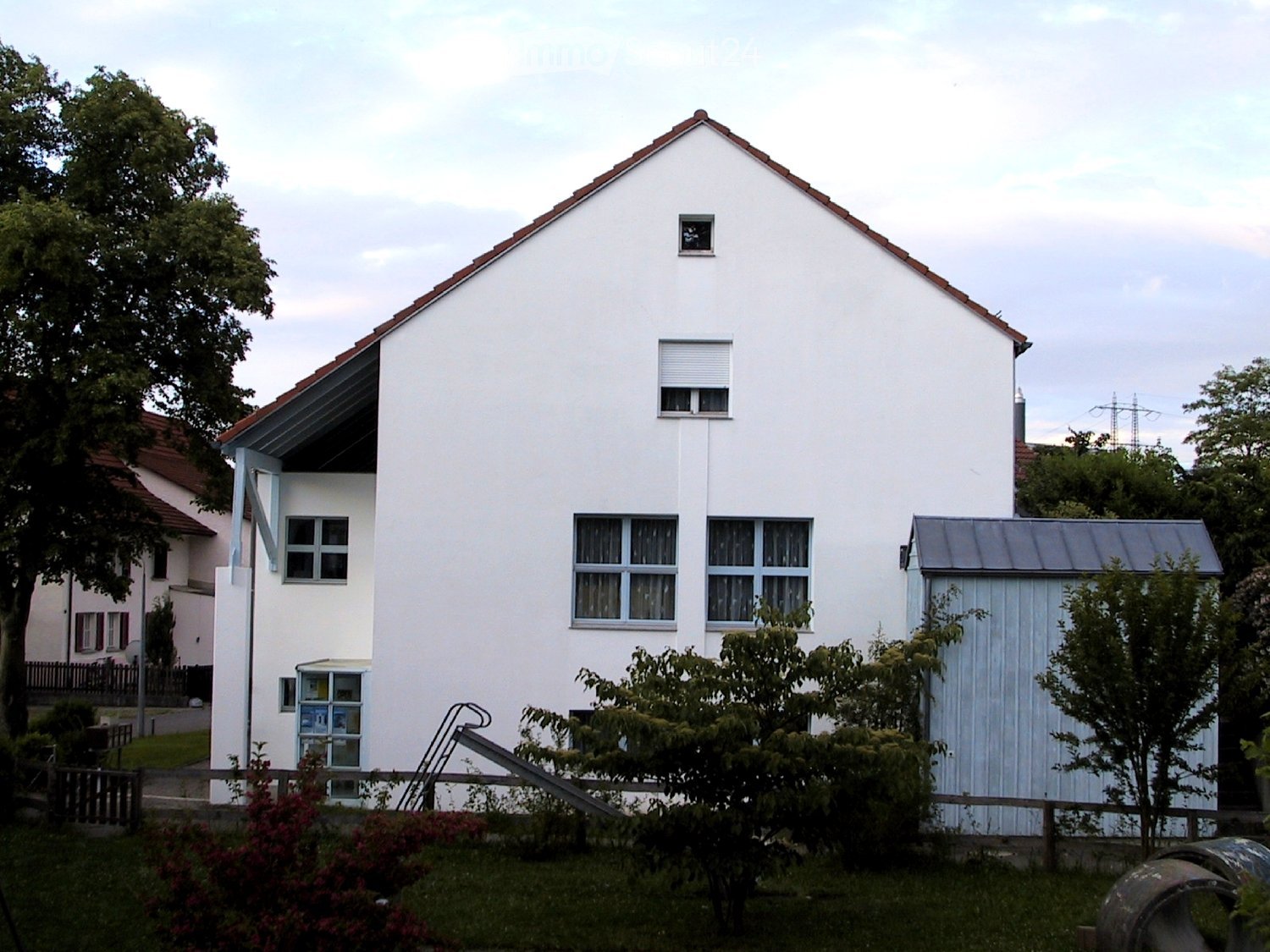 House. Two-story white house with red-tiled roof, multiple windows, small garage, and surrounding greenery.