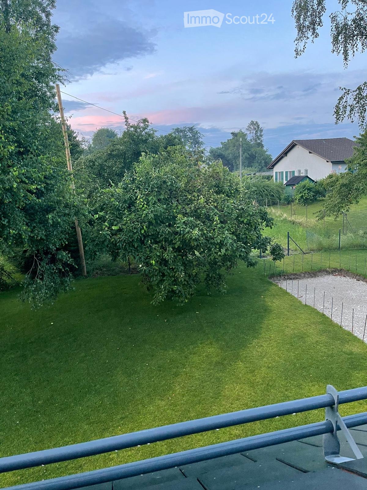 Garden / Outdoor Area. Well-maintained garden with green grass, trees, and a small house in the background.