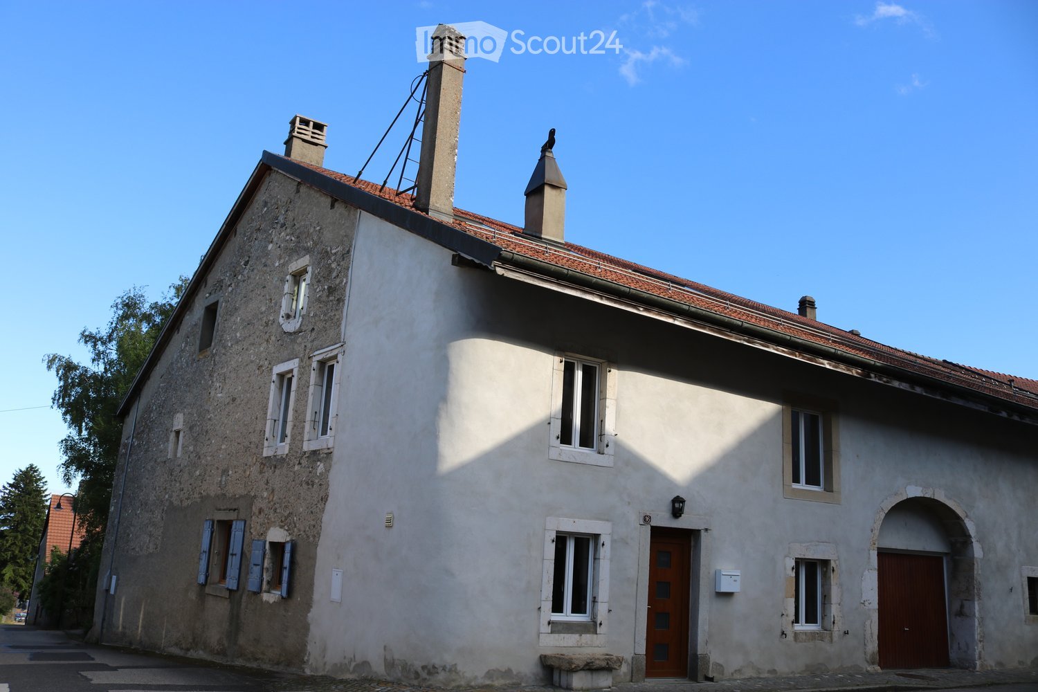 House. Two-story house with a red-tiled roof, multiple chimneys, and white-painted walls. Features include several windows with shutters, a wooden front door, and an arched entranceway.