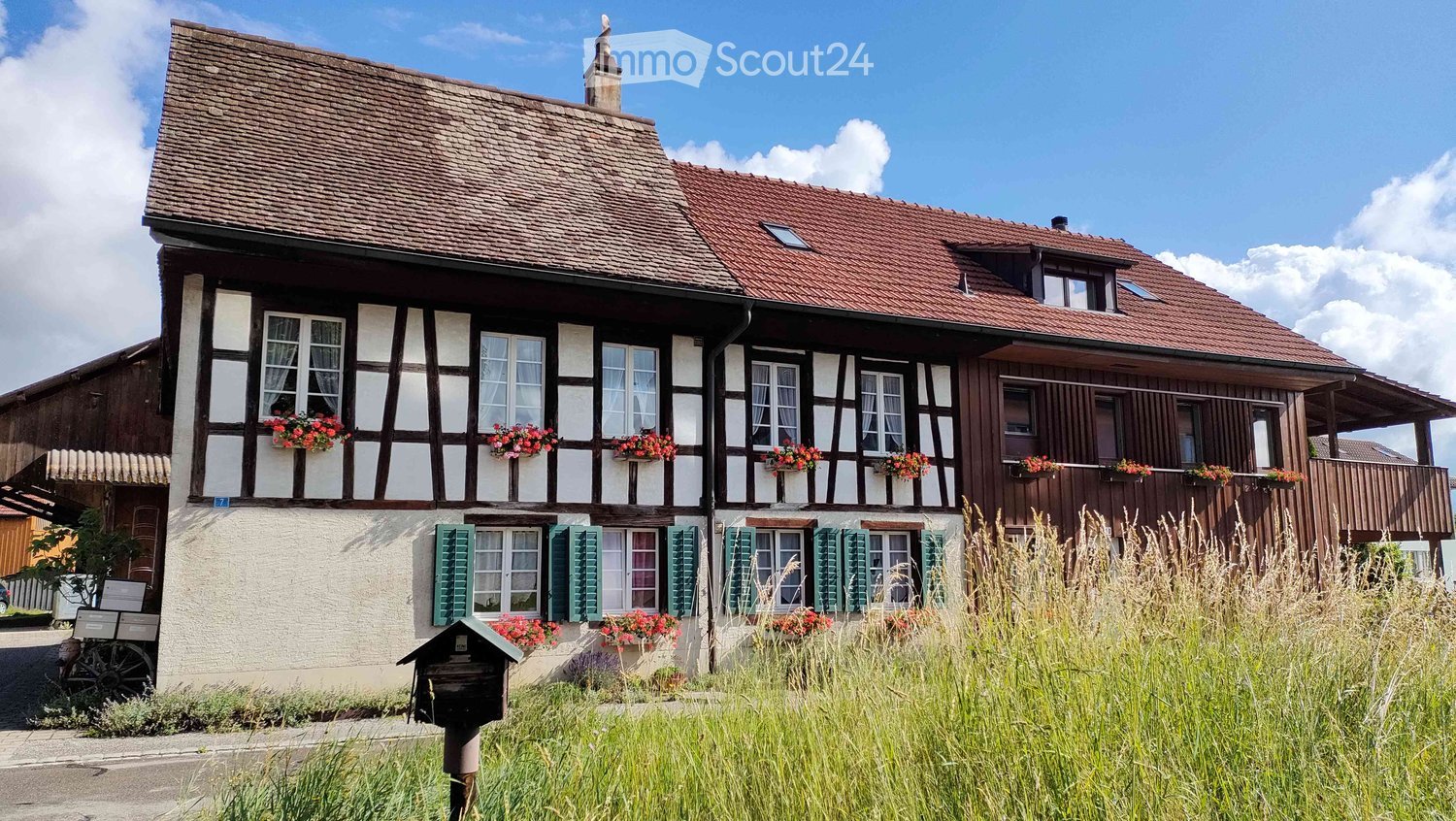 House. Traditional two-story house with a tiled roof, white and brown facade, green shutters, and flower boxes on the windowsills.