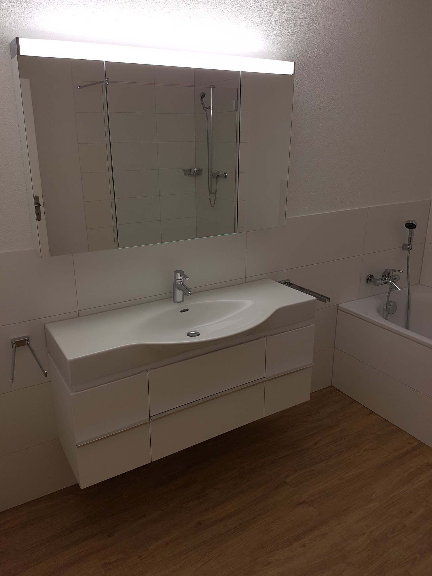 Bathroom. Modern bathroom with white sink, mirror, and cabinets. Wooden floor and white tiles.