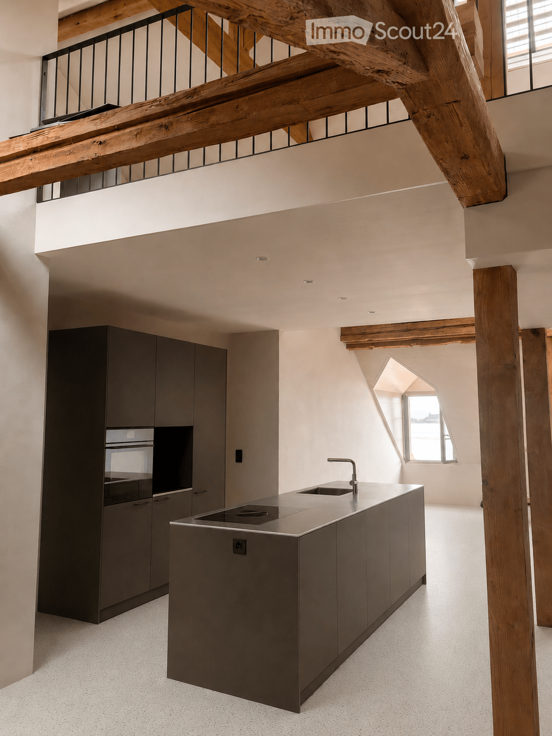 Kitchen. Modern kitchen with a central island, stainless steel sink, faucet, built-in oven, and dark grey cabinets. Exposed wooden beams and a balcony overlook the space.