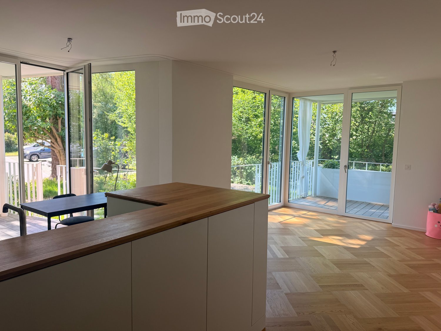 Furnished Room. Bright, modern room with large sliding glass doors leading to a balcony, wooden floor, grey cabinetry, and a wooden counter.