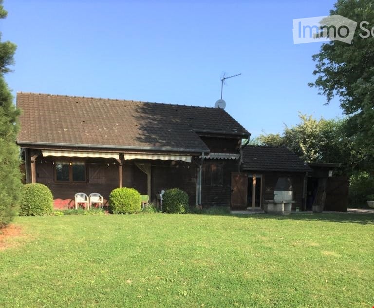 House. A two-story wooden house with a brown tiled roof, white-framed windows, and a covered porch area. The house is surrounded by a well-maintained lawn with shrubs and a few outdoor chairs.