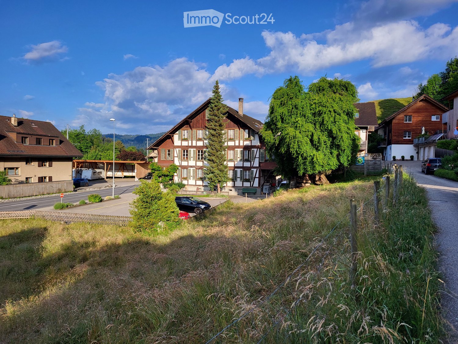 House. Traditional Swiss houses with wooden facades and pitched roofs, surrounded by greenery and a road.