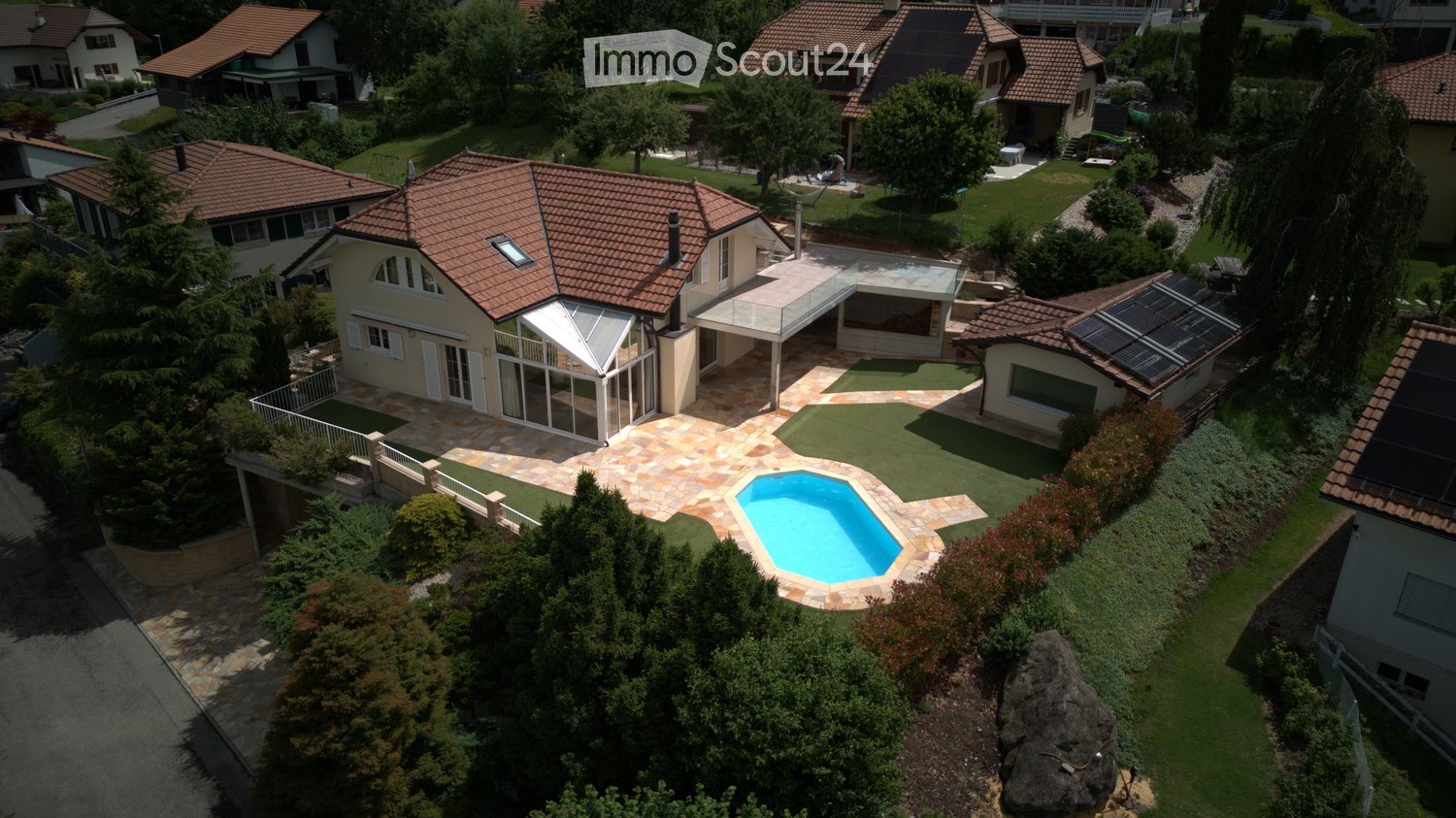 Aerial view of a residential area with multiple houses, a swimming pool, and well-maintained gardens.