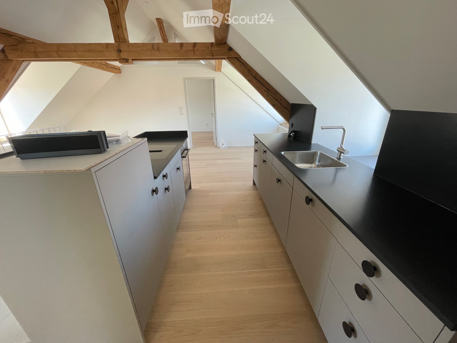 Kitchen. Modern kitchen with white cabinets, black countertops, and a stainless steel sink. Wooden flooring and exposed wooden beams on the ceiling.