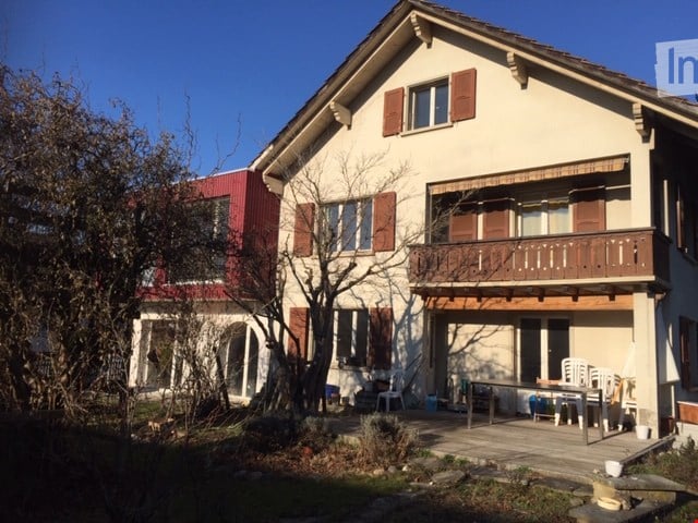 Two-story house with a balcony, red roof, and a garden in the front