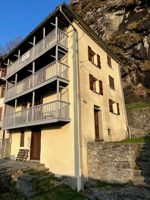 3 story building, yellow wall, balconies, small stone wall in the bottom