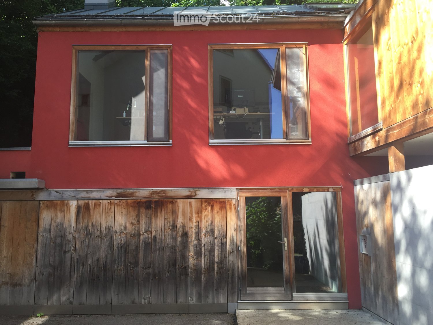Red exterior house with large windows, wooden garage doors, and a modern design.