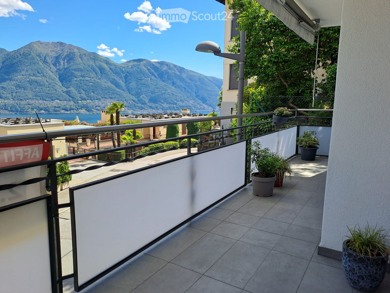 Balcony with tiled floor, white privacy screens, potted plants, and a scenic mountain and lake view.
