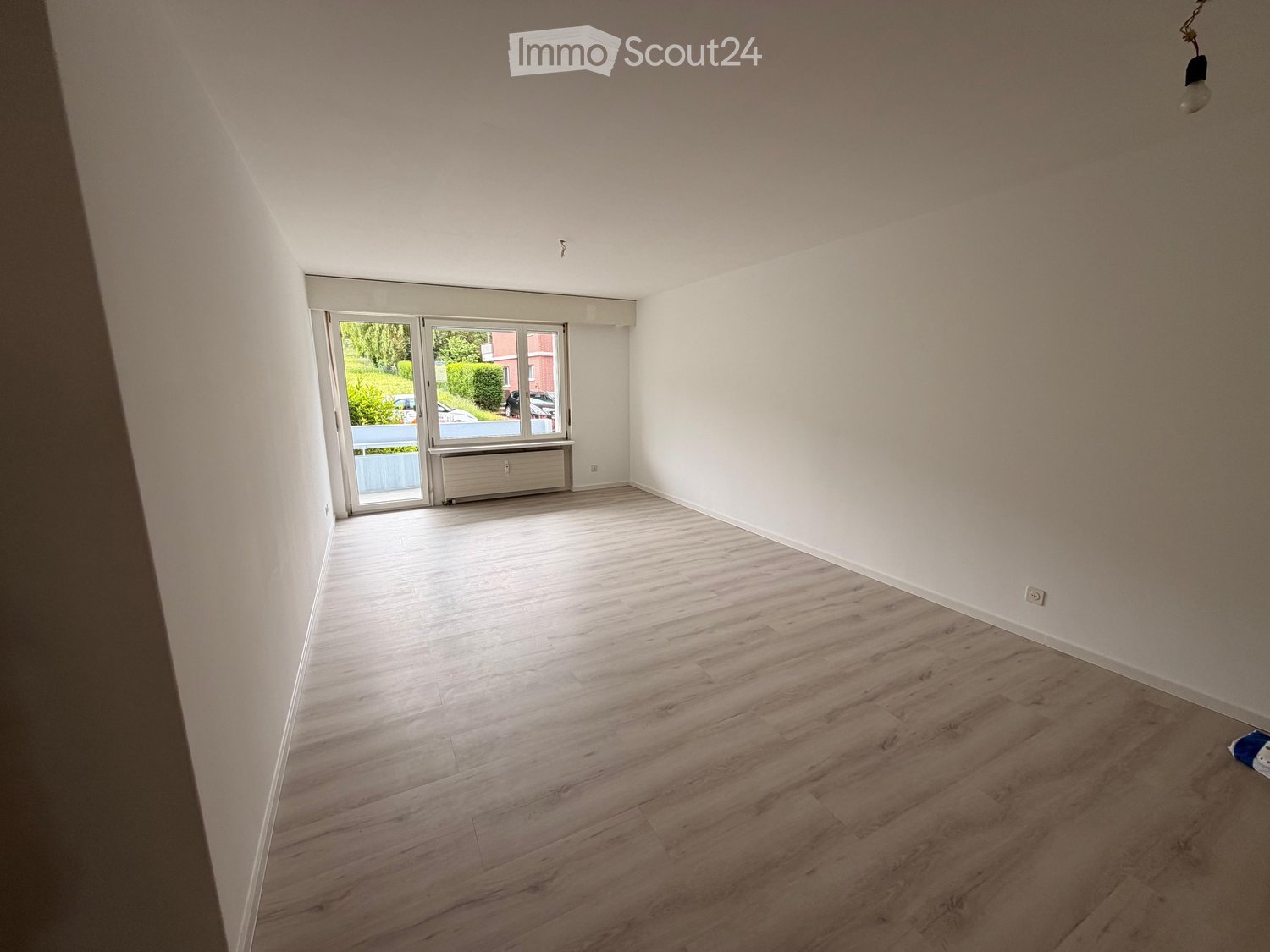 Empty room with light wooden flooring, white walls, and large windows with blinds. No furniture or equipment visible.