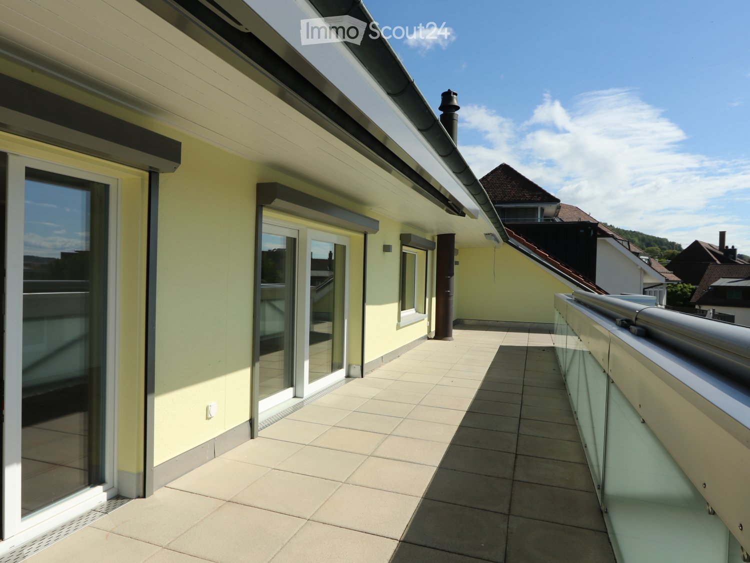 Balcony / Terrace. Balcony with tiled floor, glass railing, and access to a building with yellow walls and large windows.