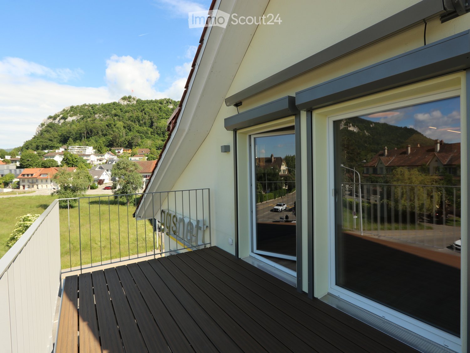 Balcony with wooden decking, metal railing, large windows, and scenic view of greenery and houses.