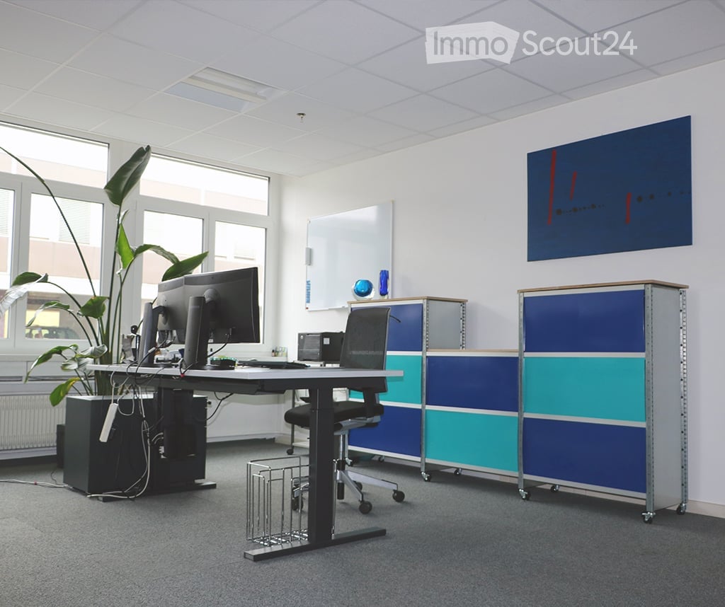 Modern office space with a desk, chair, computer monitor, potted plant, cabinets, whiteboard, and an art piece on the wall.