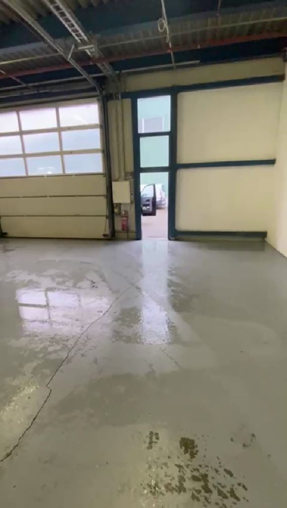 Empty garage with large roll-up door, concrete floor, and visible cracks and stains. No furniture or equipment present.