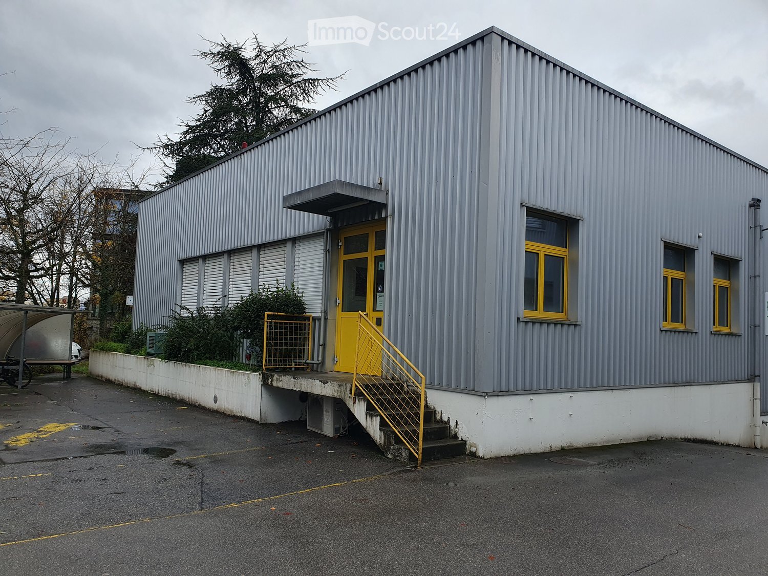 gray metal exterior, yellow door, windows, yellow railings, concrete pavement