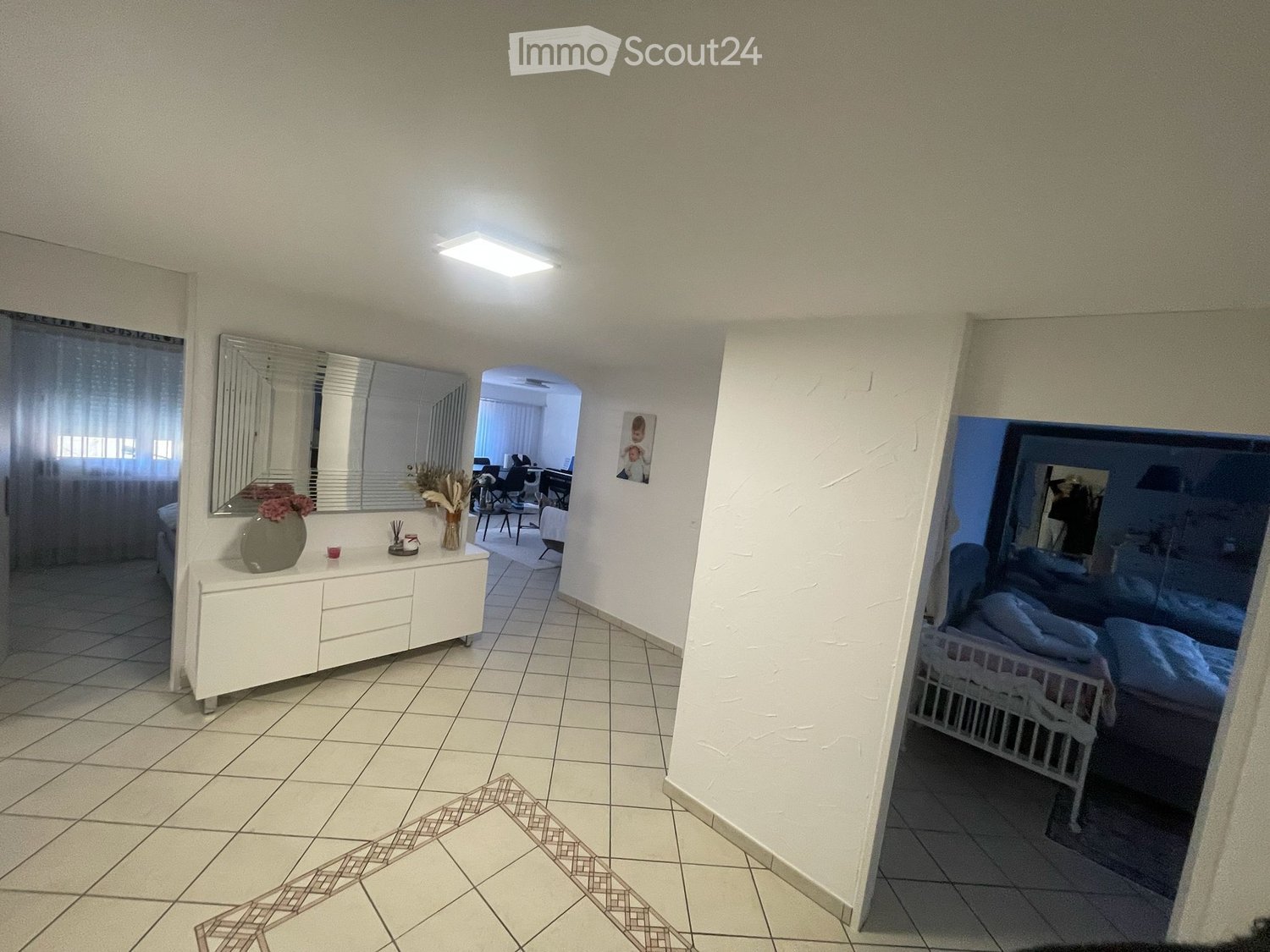 Furnished Room. A furnished room with a dresser, vase, mirror, and a visible bedroom area with a bed and chair.