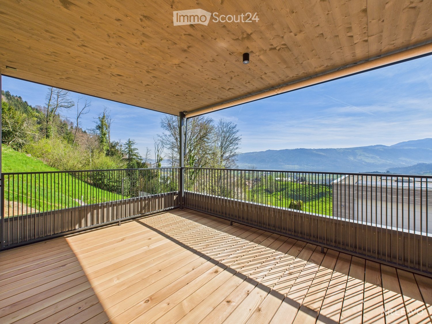 Wooden deck with black metal railing, offering panoramic mountain and valley views.