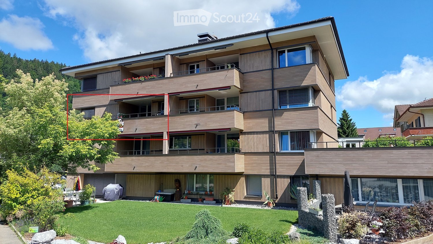 Modern multi-story apartment building with balconies, large windows, and a well-maintained garden area in front.