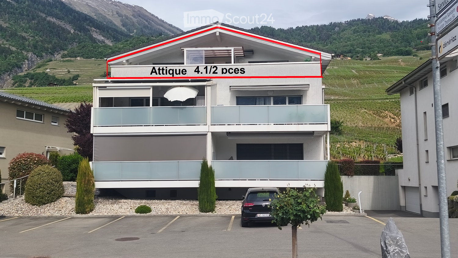 Modern two-story house with large windows, balconies, and a parking area. The house is situated in a scenic area with vineyards and mountains in the background.