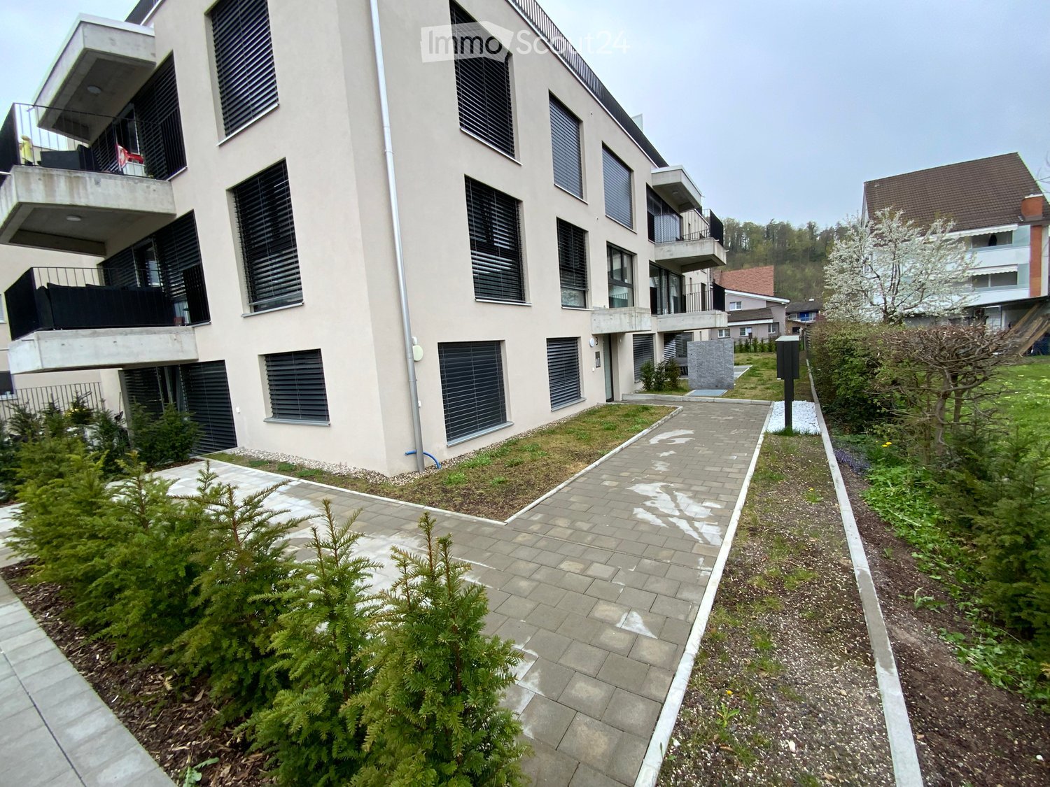 Modern multi-story residential building with balconies, large windows, and surrounding greenery.