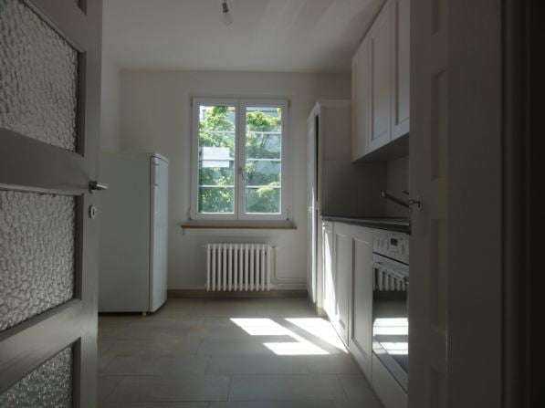 Empty kitchen, tiled floor, white appliances, window, cabinets, radiator