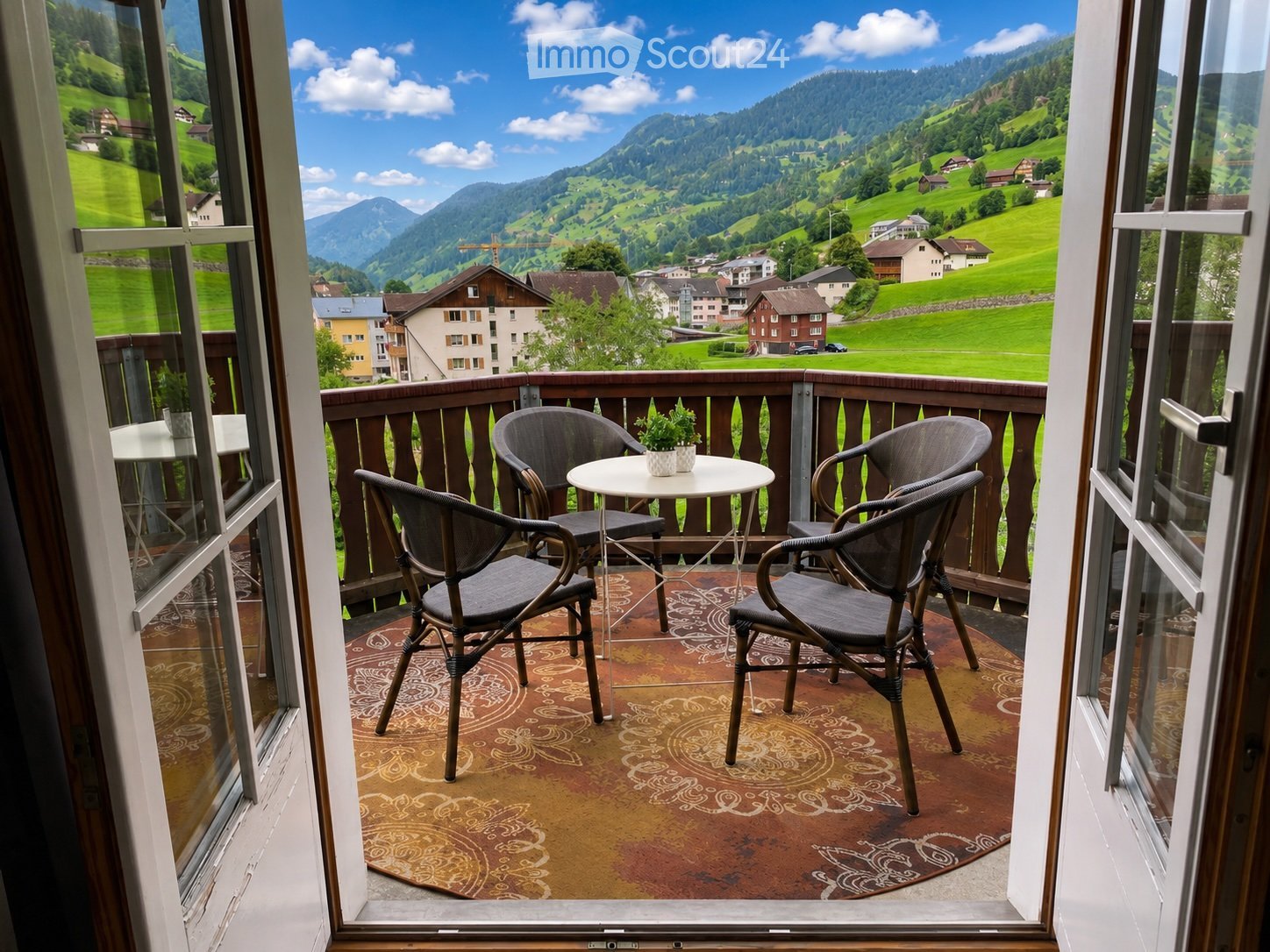 Balcony with a scenic mountain view, featuring a round table, four chairs, and a patterned rug.