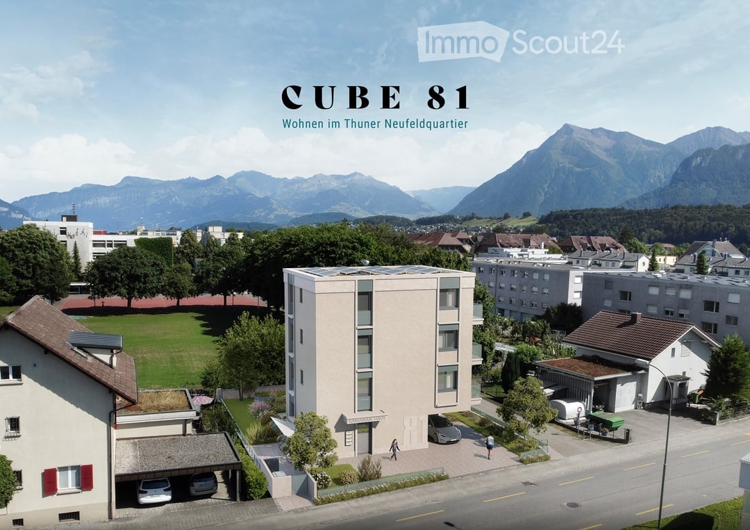 A modern multi-story residential building labeled "CUBE 81" in a suburban area with surrounding houses, green spaces, and mountain views.